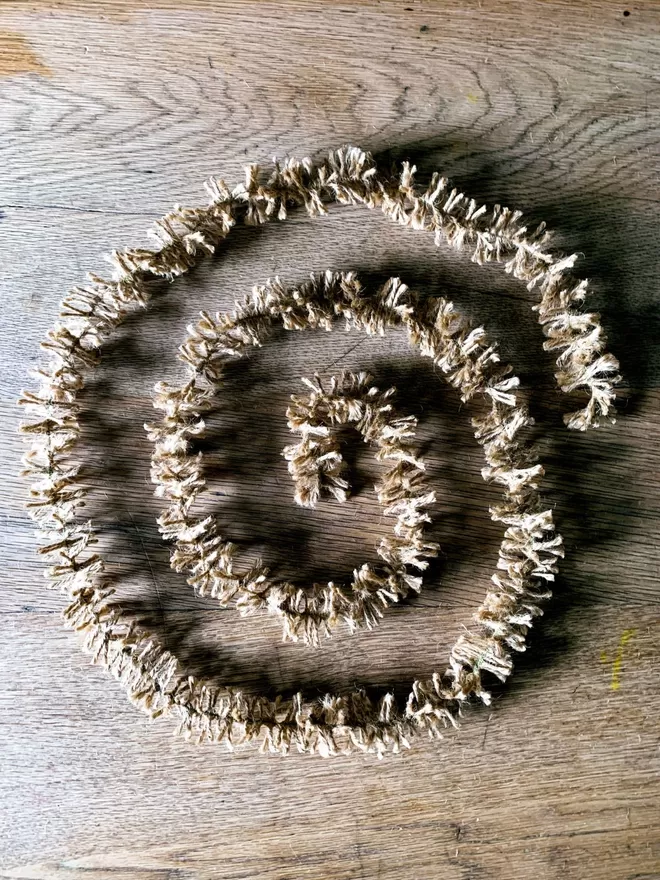 Undyed golden jute string tinsel AKA Strinsel laid out in a spiral on an oak table