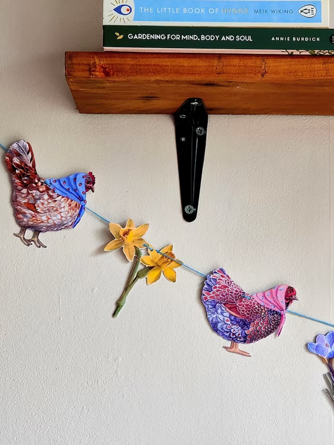 illustrated easter chickens and spring flowers garland. chickens wearing easter bonnets on bunting, hung on a wall.