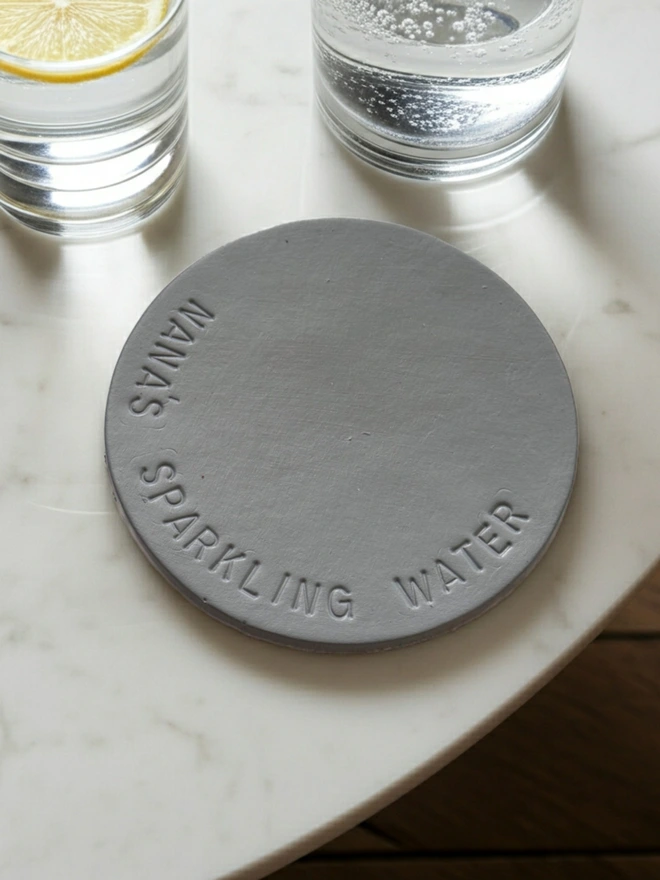 grey leather coaster with Nana's Sparkling Water stamped on it.