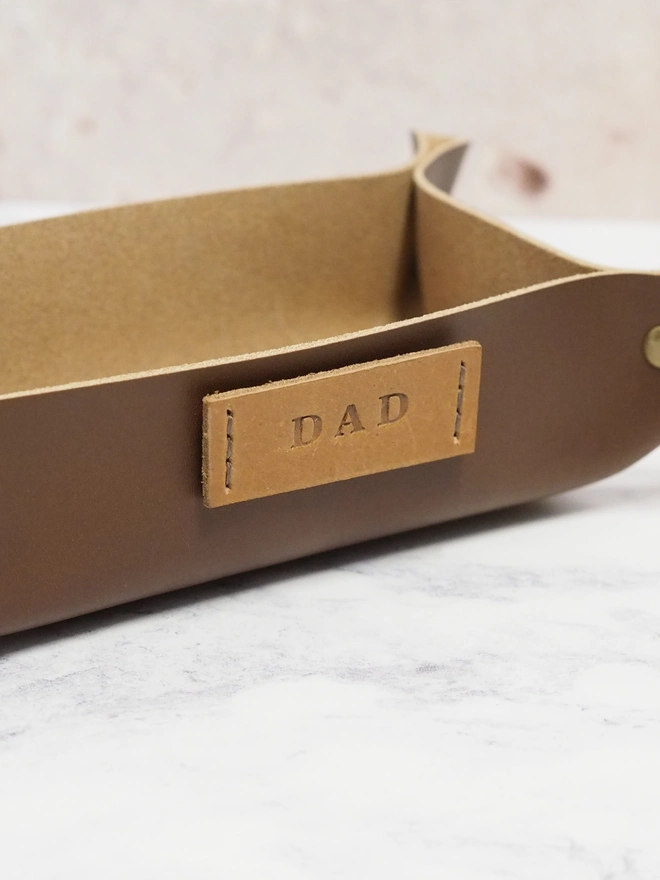Personalised leather tray. A close up of a handmade leather coin tray with a personalised name tag.