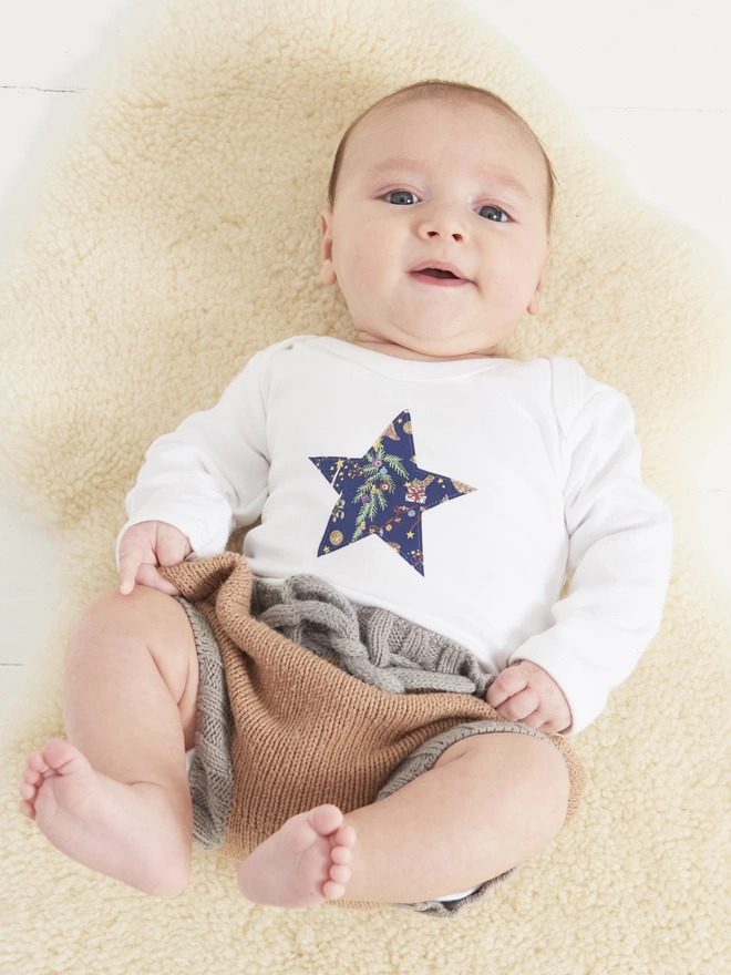  A baby wearing a bodysuit featuring a star in Liberty Christmas festive print