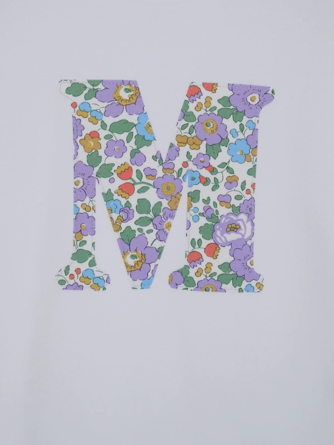 a personalised kids white t-shirt with an initial cut from betsy purple liberty floral print on the front. A close up of the stitching.