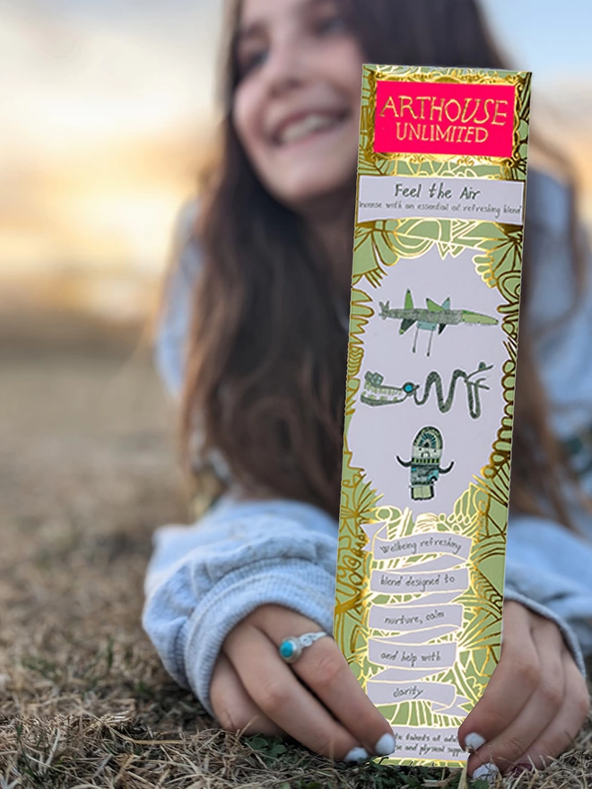 girl in a field feel the air well being charity incense sticks with gold & green illustrations