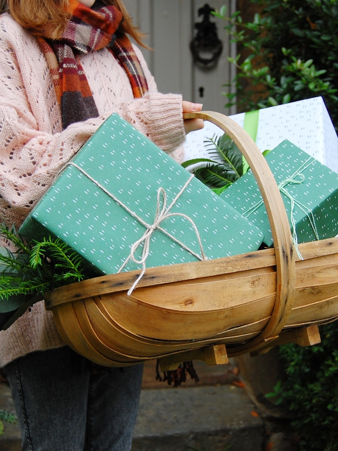 A basket full of gifts wrapped in white and green wrapping paper with a tiny tree design.