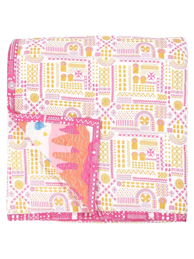 Fairy Chimney Quilt, a pink and yellow quilted bedspread folded on a white background.