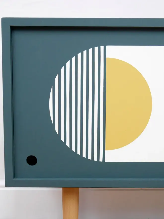 Teal mid-century record cupboard with sliding doors featuring bold geometric patterns in white and yellow.