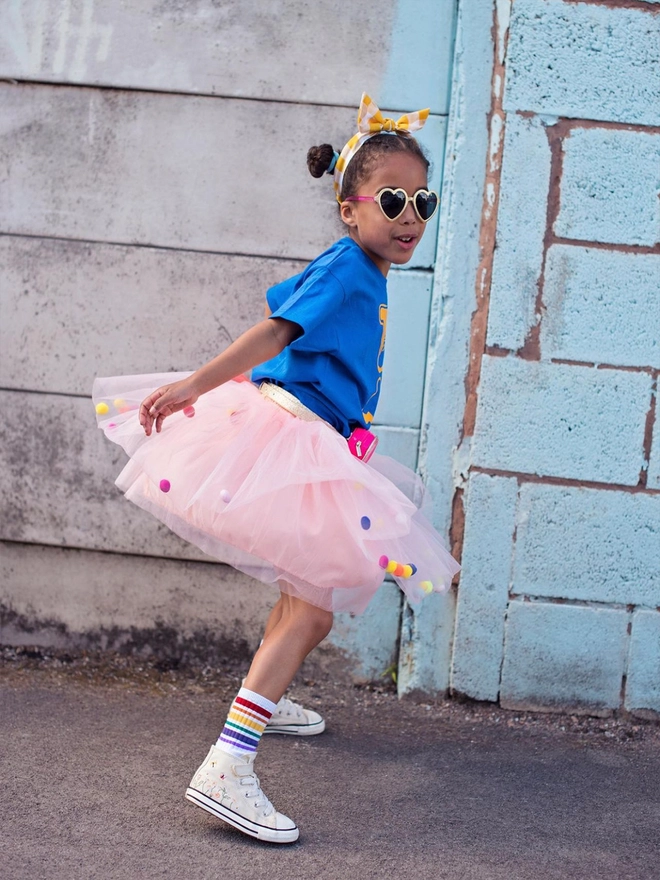 Girl wearing a peach tutu with neon pom poms twirling in front of a wall.