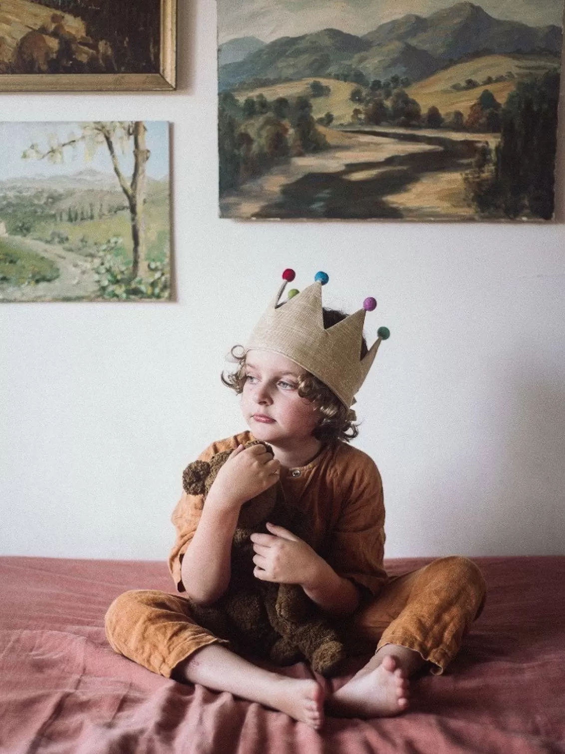 Child seated on a bed wearing the Old Gold Pom Pom Crown.