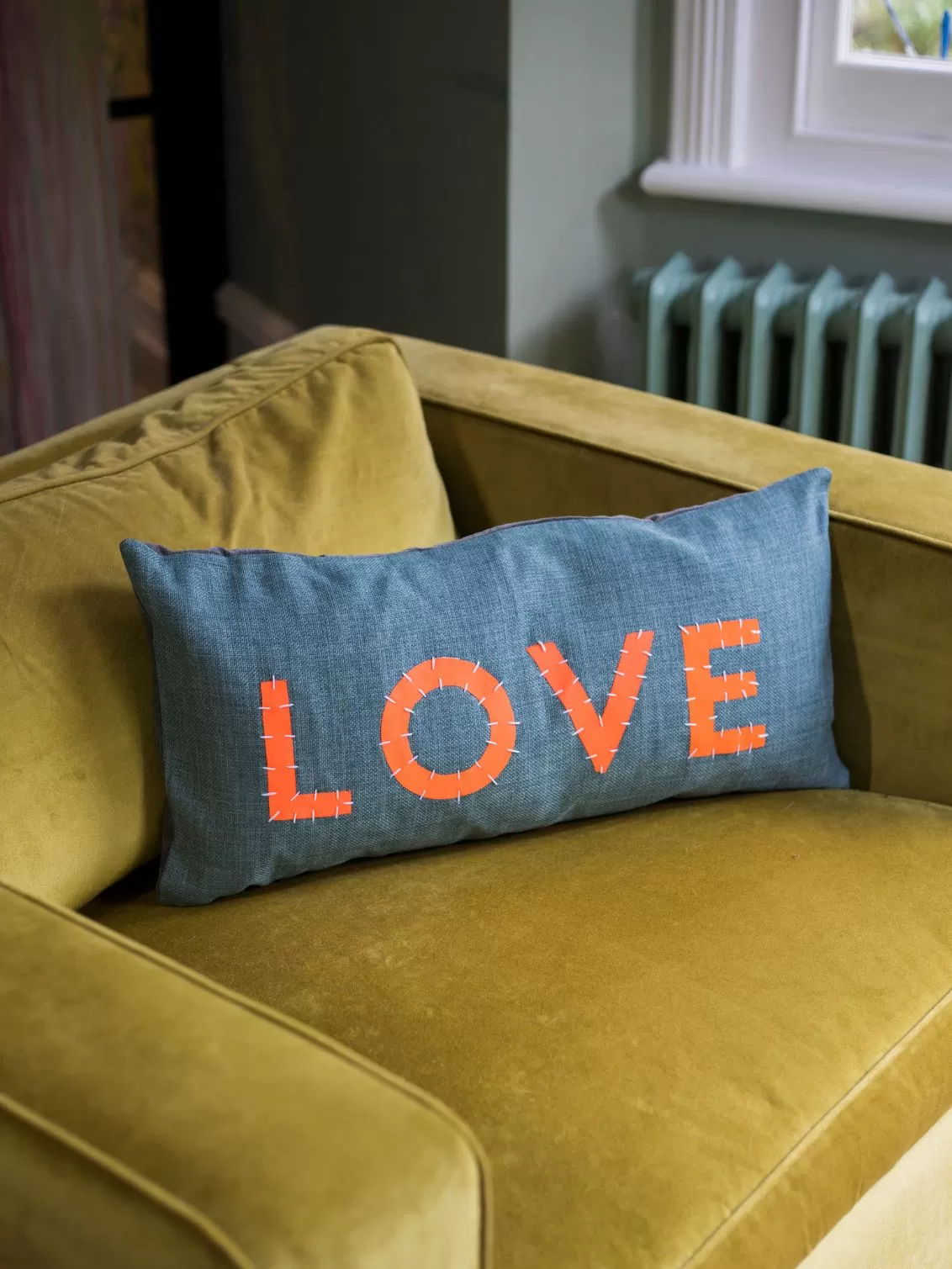 Love welcomes Love cushion seen on a yellow sofa.