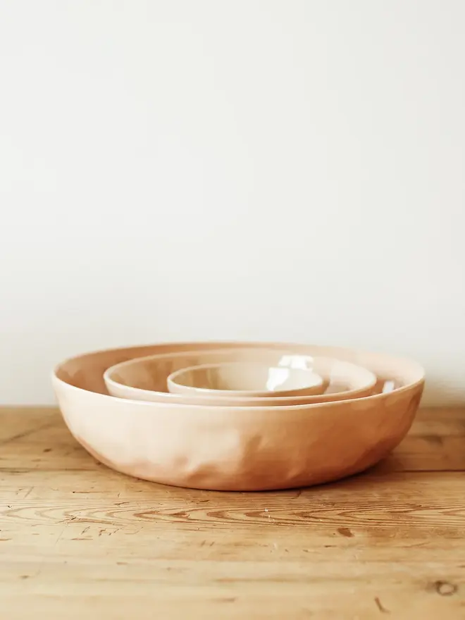 'sunrise' handcrafted stoneware bowls. a set of three pink bowls on a wooden bench.