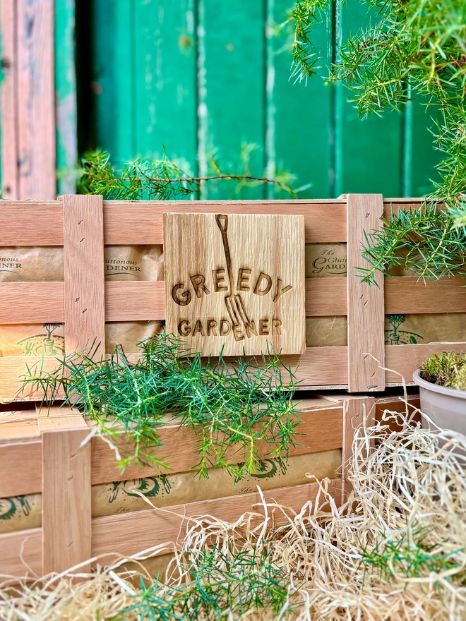 The Greedy Gardener Logo engraved onto a wooden plaque and attached to a wooden gifting crate