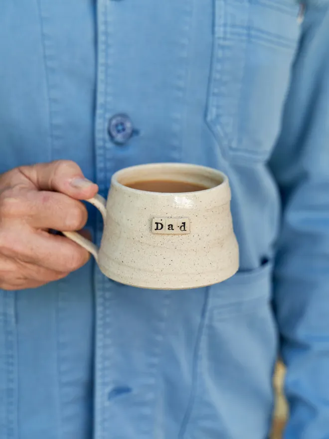 Personalised mug- 'Dad' held up against a blue shirt 
