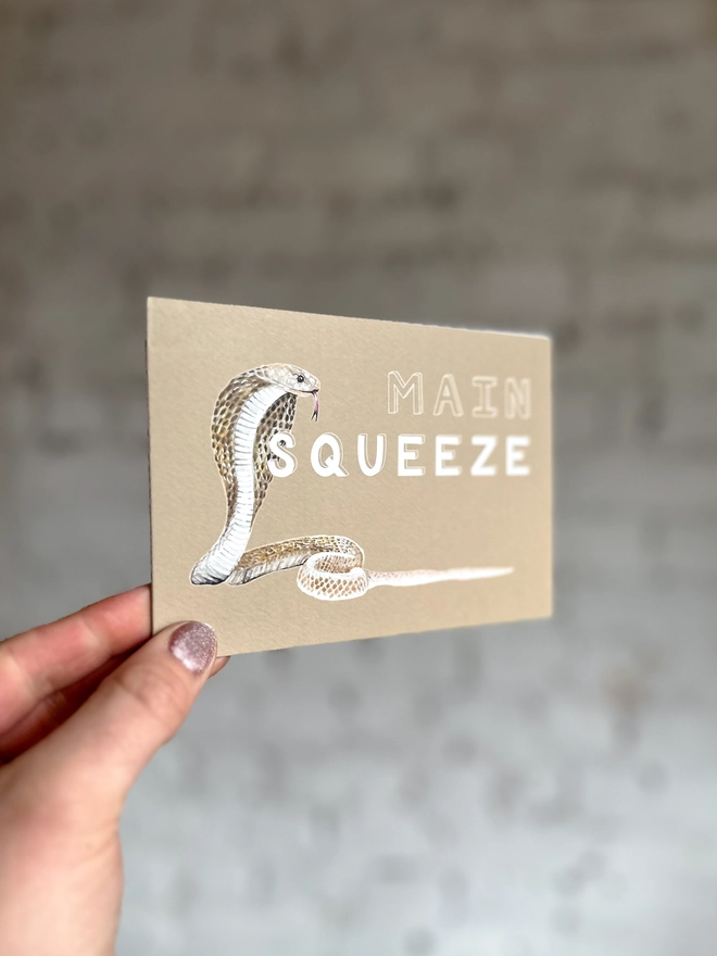 a beige greetings card featuring an illustration of a cobra with the text “main squeeze”
