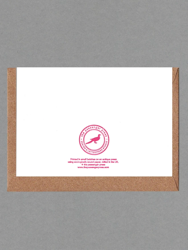 Back of white card with pink text with brown envelope behind