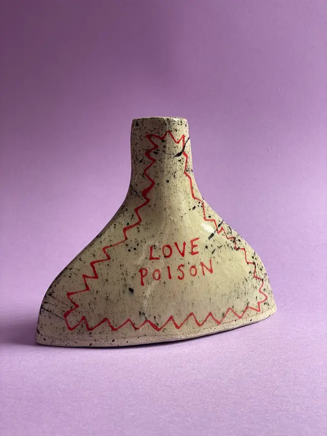 Love Potion/ Poison Bottle Vase, a vase that says 'love poison' in front of a purple backdrop. Each is stamped with a signature red dot on the bottom. 