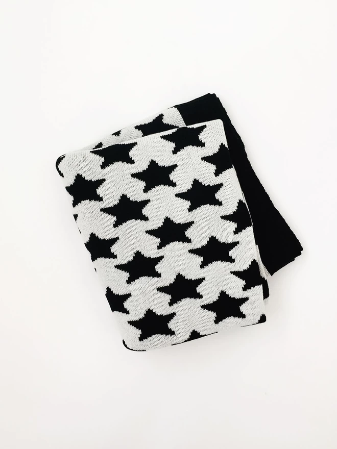 A folded junior blanket, photographed from above, showing a black and white star pattern and a glimpse of black trim.