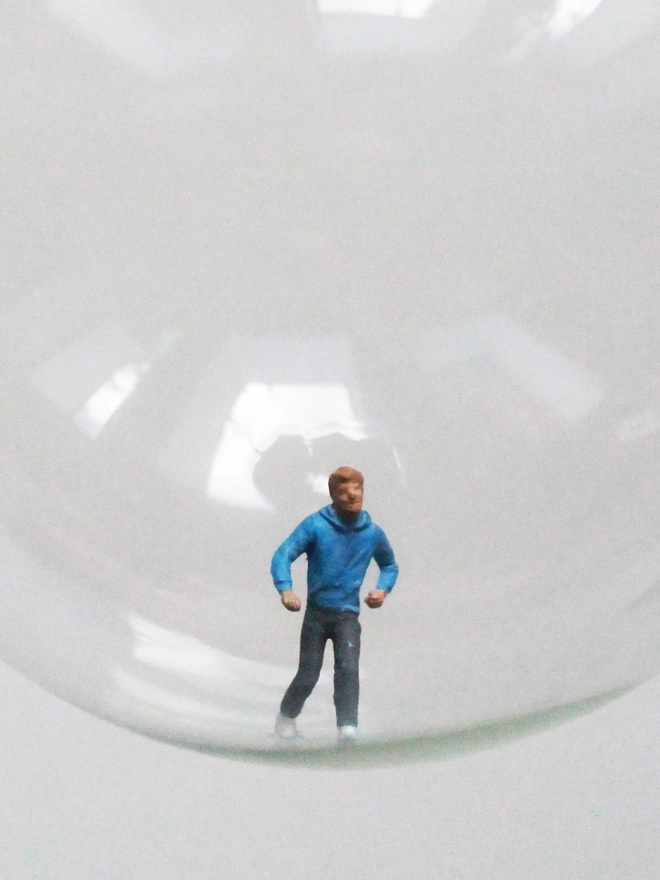 Miniature figure of a man running in a glass Christmas bauble - close up 