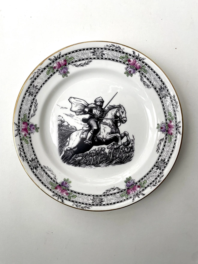 a knight on horseback rides through the woods, the image is victorian in black and white and is printed directly onto an ornate vintage plate