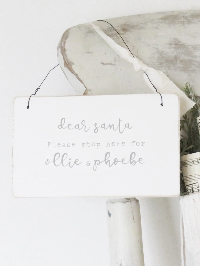 painted white sign with personalised festive message strung with wire and decorated with ribbon.