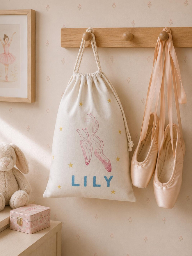 personalised ballet bag. a drawstring ballet bag with a personalised name hanging up next to ballet shoes.