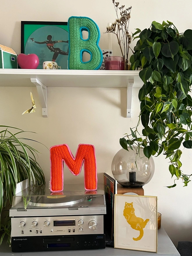 Crochet cushions shaped like the letters B and M displayed stood up in a living room