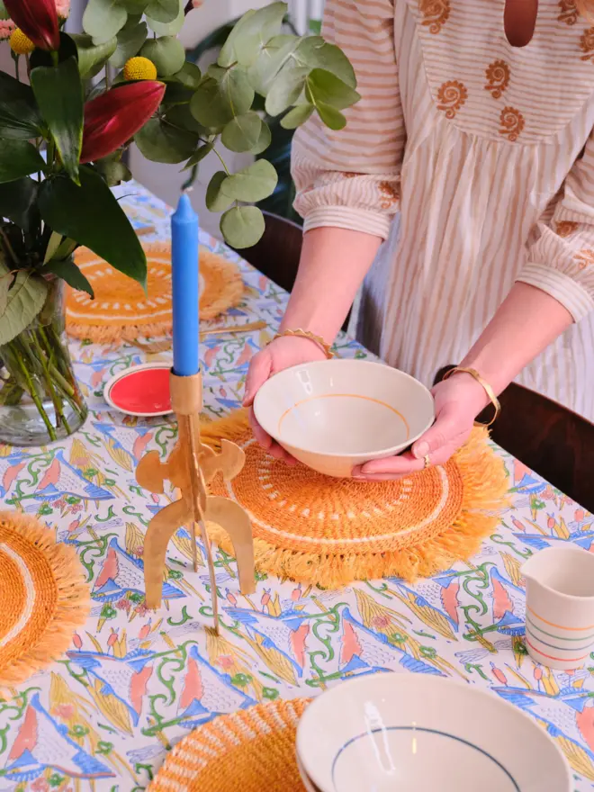 A yellow fringed placemat sitting on top of a colourful tablecloth