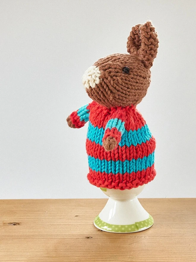 Egg Cosy Rabbits Easter Table Decoration, an Easter cosy sitting on a wooden surface. 