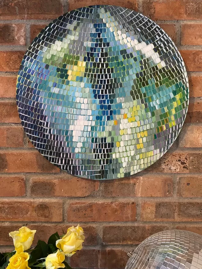 a large round painting on a brick wall background with yellow roses at the bottom left