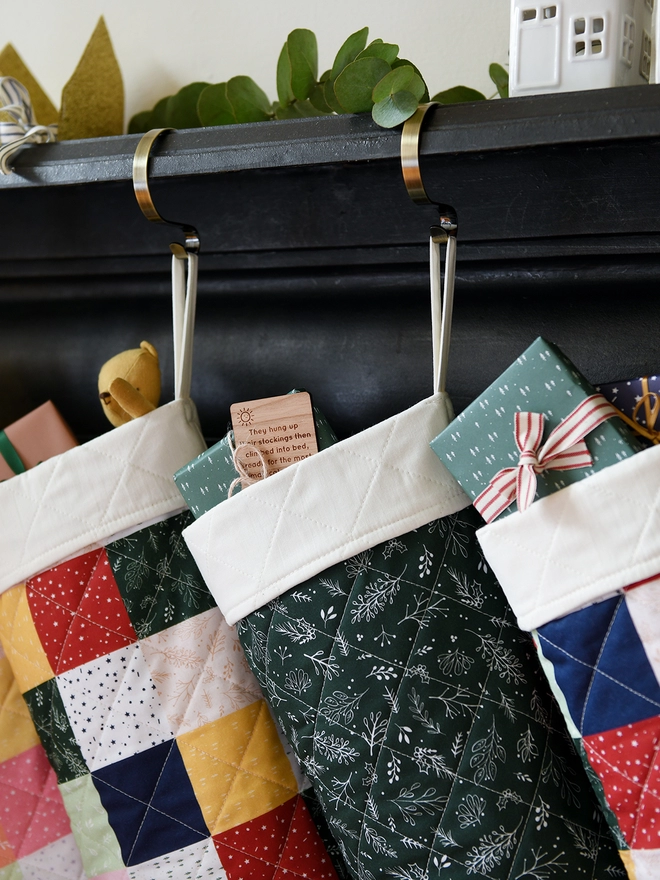 Three quilted patchwork stockings hang from a black mantlepiece. Small gifts and toys poke out of each stocking.