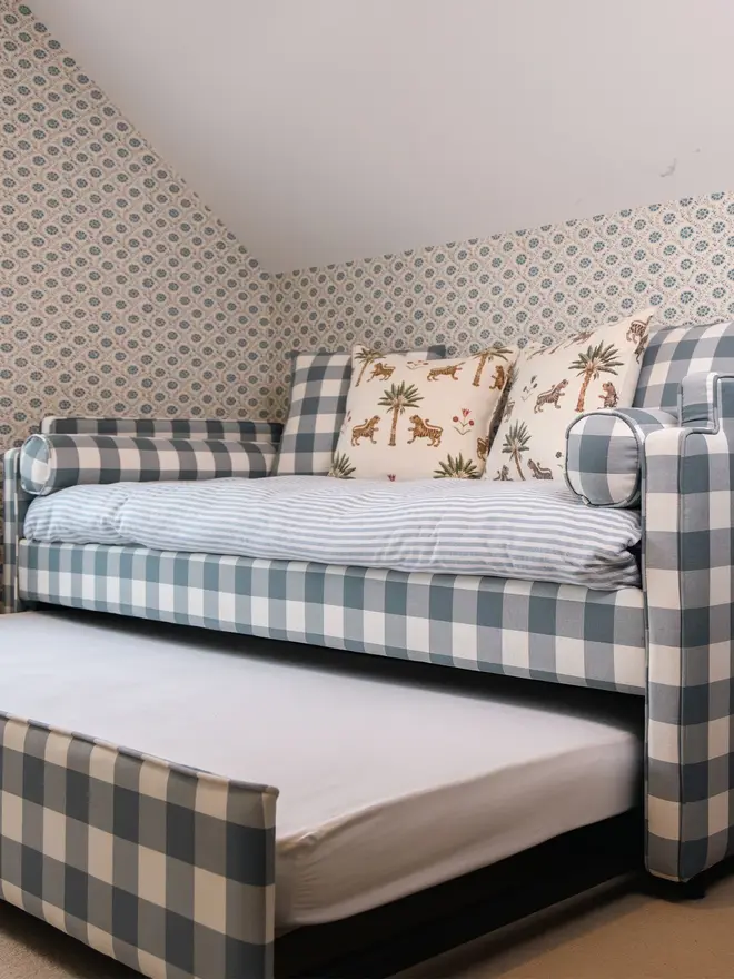 'The Posie' blue gingham upholstered children's bed. a blue gingham sofa-style bed for children featuring a duvet and cushions with the bottom trundle bed pulled out.