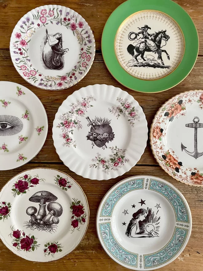 an eclectic collection of vintage plates hung together on a wood wall, each plate is different with patterned or gold borders and vintage images in their centres