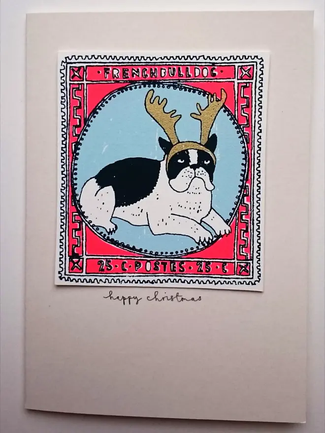 Happy Christmas French Bulldog Card, a white card with a colourful dog design in the centre on a white surface. 