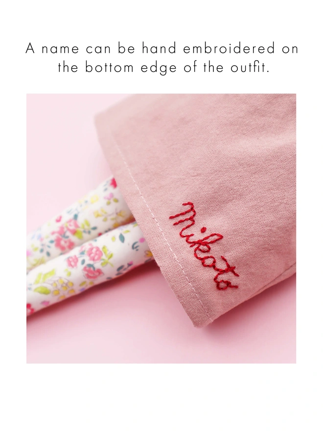 A name handembroidered on a doll's dress along the hem.