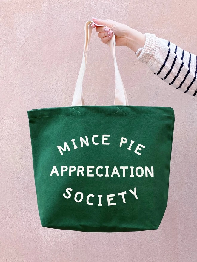 Hand holding out the Green canvas Mince Pie Appreciation Society tote bag