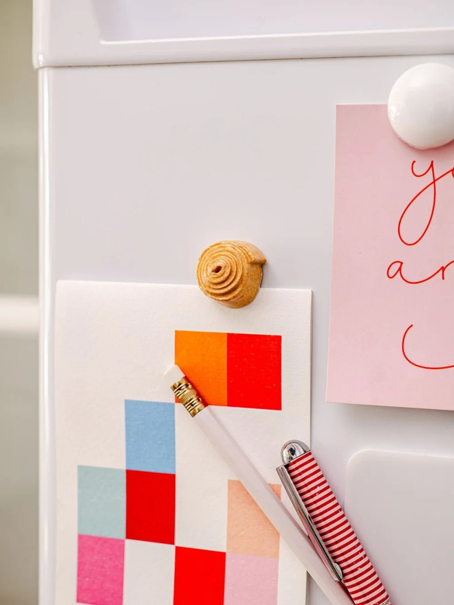 ceramic pastry magnets. a ceramic cinnamon bun magnet on a fridge door.