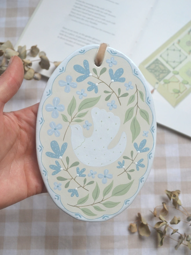 oval ceramic decoration with white dove illustration and blue and green floral decor