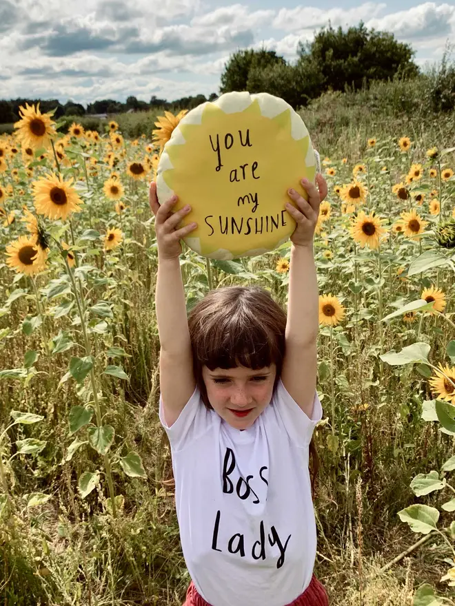 Girl holds plushie above her head, in field of sunflowers