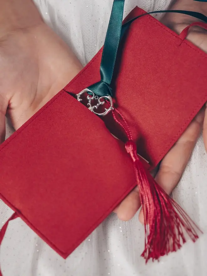 An open red suede pouch holds the silver key. Its green ribbon and red tassel spill out over the edge.