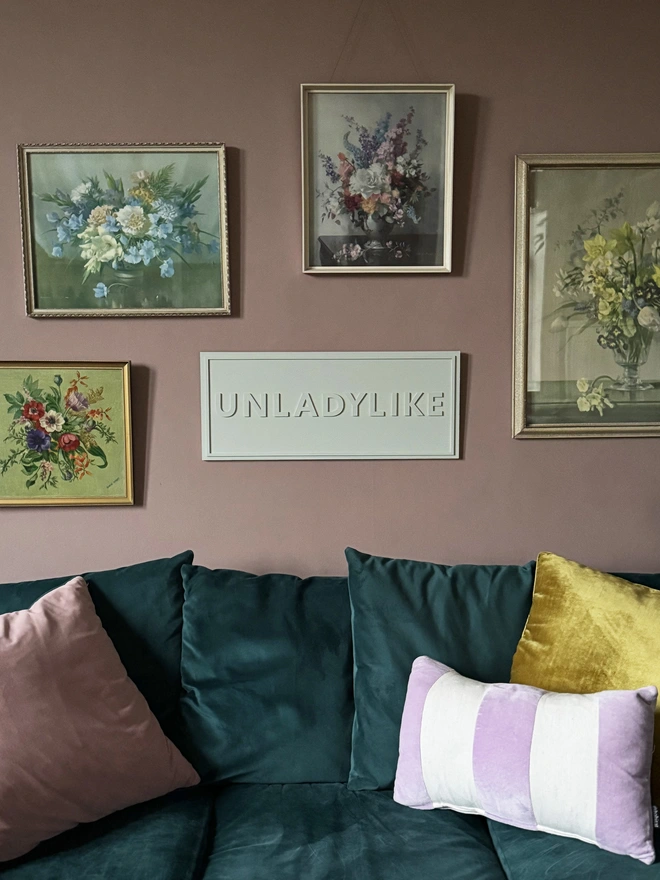 soft green painted sign reading unladylike in a formal sitting room setting, with pink walls and velevt green sofa