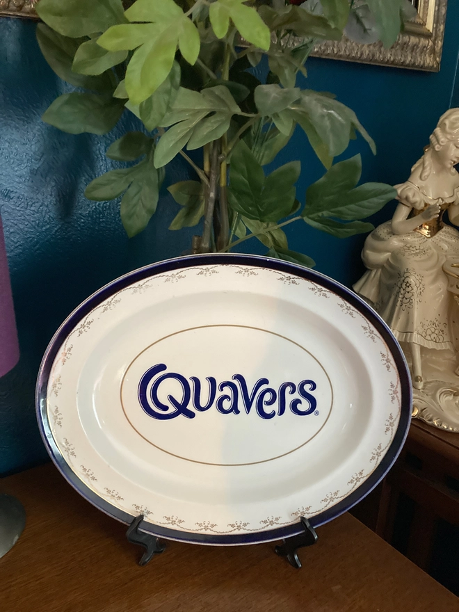 oval vintage china plate with a navy rim, featuring a navy blue 'Quavers' logo across the centre.