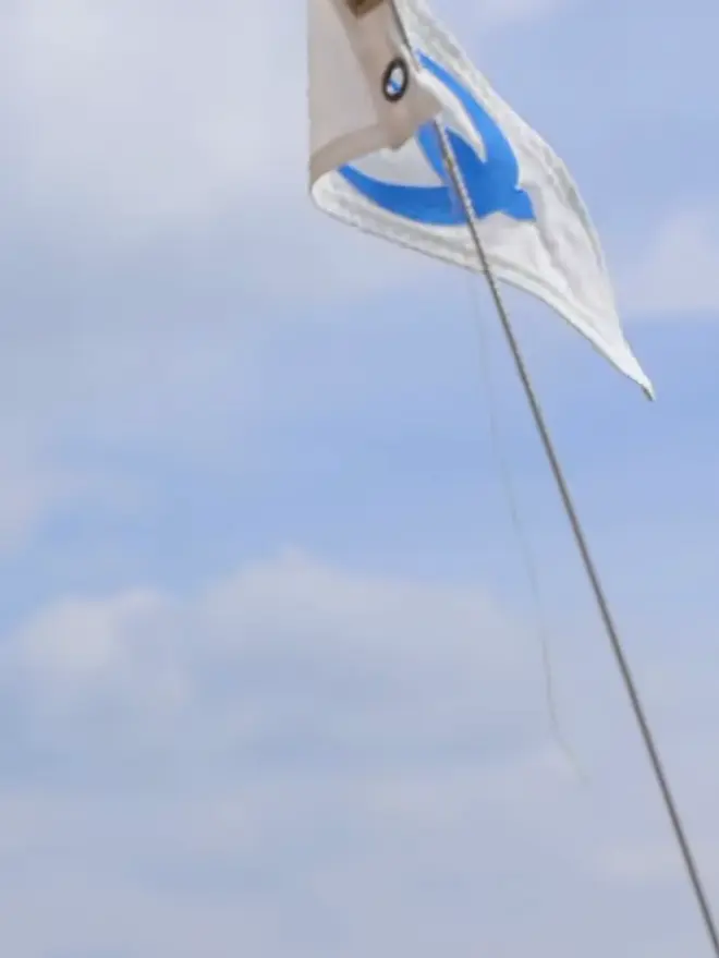 An ivory pennant flag with a blue stitched on swallow bird flying from a boats mast