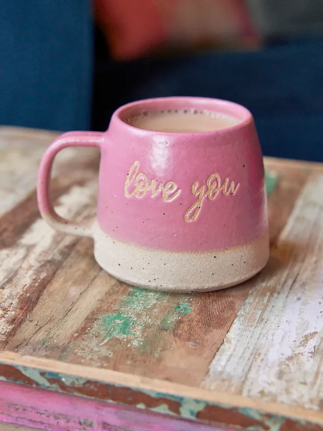Love you pink ceramic mug. A pink mug with love you written on the front placed on a wooden surface.