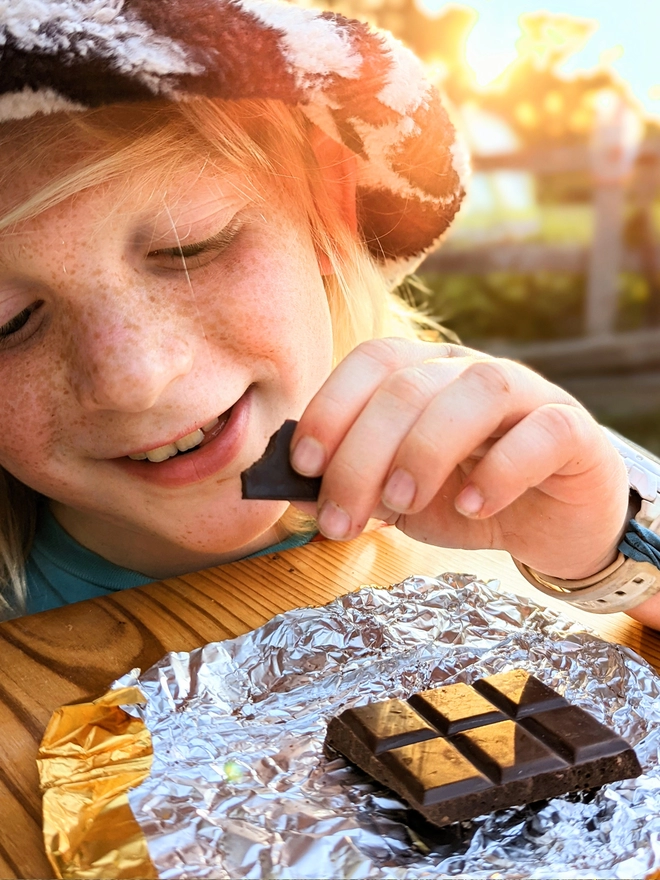 Happy young child opening gold foil wrapped charity dark chocolate with honeycomb bar