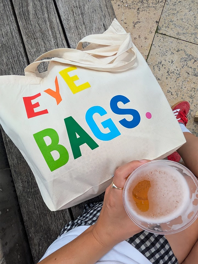 A natural coloured tote bag with multi coloured 'Eyebags' slogan