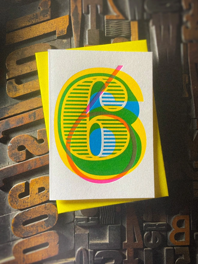Handmade letterpress 6th birthday card featuring bold overlapping numerals printed in vibrant fluorescent cyan, magenta and yellow inks. Each card is individually hand printed using traditional letterpress techniques on luxury paper stock, creating a beautifully tactile finish with a deep impression and rich layered colours inspired by the CMYK printing process. Printed on a traditional letterpress from 1915.