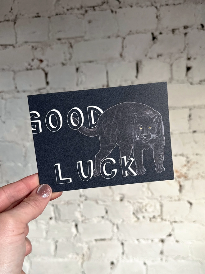a dark grey greetings card featuring an illustration of a black panther with the text “good luck”
