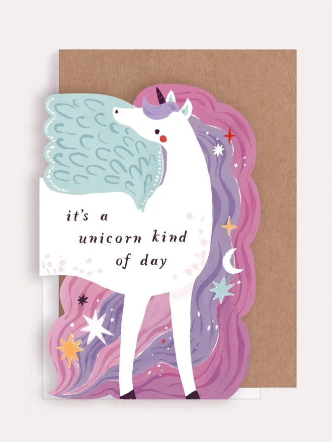 Unicorn shaped birthday card with a pink and purple mane of stars and moons, with a kraft envelope
