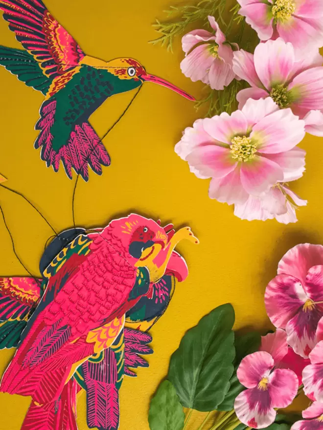 Close up of the tropical pink birds behind a yellow background and pink flowers