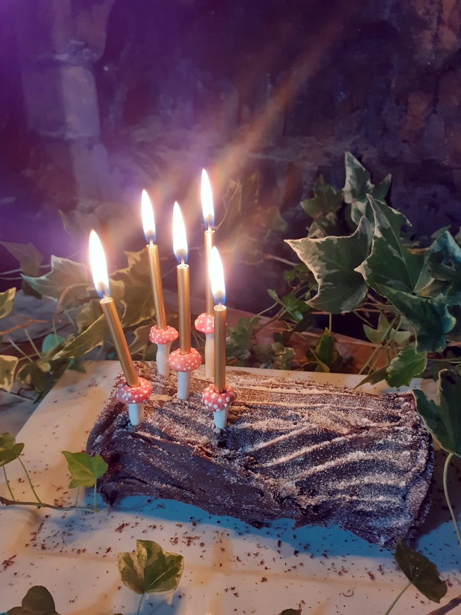 Close-up of five handmade ceramic toadstool cake candle holders, showing their glossy white stems and individually spotted red caps beneath lit gold candles.