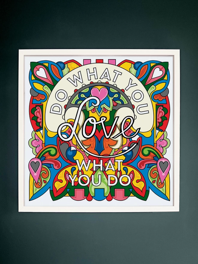 “Do what you love, love what you do” is written over a vibrant, rainbow coloured illustration. The picture is hanging in a white square frame on a dark grey wall. 